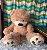 Full view of the tan plush teddy bear seated upright highlighting size and features including paws and face.