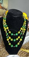 Three strand necklace with multi-shade green beads displayed on a black velvet bust stand.
