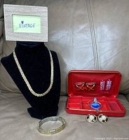 Vintage jewelry case open showing interior red velvet and satin compartments with earrings and pendant inside.