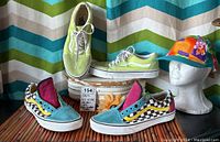 Pair of vintage Vans shoes in green neon leather and suede with floral and blue checkerboard details, displayed with multicolor floral cap on mannequin head and chevron background fabric.