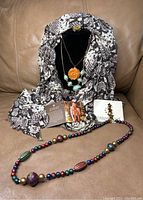 Python print scarf arranged on couch with necklaces and pin displayed inside and in front, showing variety of accessories in the lot