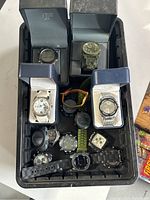 Overall lot of 12 watches in a black container showing varied conditions from heavily used with deteriorated rubber straps to watches still in display boxes.