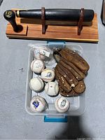 Lot overview showing vintage glove, multiple baseballs in plastic bin, and wooden bat display shelf holding a black bat
