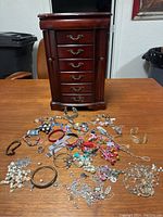 Image showing 17-inch dark wood jewelry armoire with six drawers and costume jewelry spread in front including bracelets, necklaces, rings, and a watch.