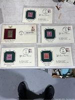 Five first day issue stamps mounted on commemorative envelopes, each in clear protective sleeves, laid out on the floor.