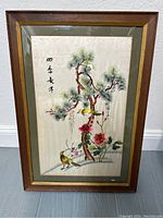 Framed textile needlework artwork showing entire piece inside wood frame with green inner mat board