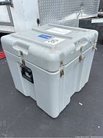 View of large, square shaped, light gray plastic storage container with metal buckle locks on sides and black handles for transport. Shows overall shape and condition.