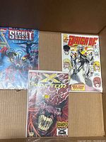 Three comic books including Topps Secret Saga, Marvel X-Factor, and Brigade comics inside a cardboard box.