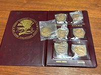 Photo of the maroon folder holding seven sealed collectible coins labeled with different North American hunting game animals.