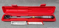Torque wrench inside its red plastic carrying case along with instruction pamphlets.
