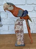 Front view of carved stone parrot figurine with painted body perched on cylindrical marble base.