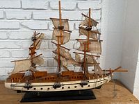 Full sideview of the wooden clipper ship model on a black stand, showing three masts with multiple fabric sails and rigging.