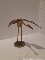 Front view of solid brass crane statue showing outstretched wings and long legs on circular base