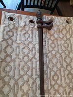 Curtain panel laid flat with metal grommets and geometric pattern visible next to part of the extendable curtain rod with decorative finial.