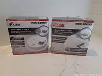 Two sealed Kidde Pro Series smoke detector boxes shown side by side on a marble surface