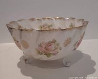 Side view showing floral pattern, scalloped rim, and three scroll feet base of porcelain bowl.