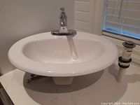 White round sink with attached chrome single lever faucet shown from an angled top front view. Sink is mounted with visible plumbing underneath.