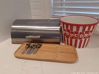 Wide shot of the breadbox, popcorn bowl, bamboo tray and four Christmas spreaders placed on a white counter.