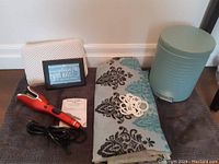Full lot including Chi hair curler, bath headrest, shower curtain with hooks, bath mat, trash can, and framed postcard arranged on floor.