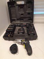 Craftsman cordless drill kit in black molded case showing drill, two batteries, and charger, plus Power It hand drill with power adapter outside case on white surface