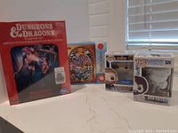 Dungeons & Dragons Stranger Things Starter Set sealed box, Bob Ross and Captain America POP vinyl figures in boxes, and Zelda puzzle box on countertop.