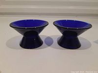 Pair of blue cobalt glass candle holders shown side by side from the front, highlighting shape and color.