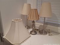 Three bedside lamps and one large lampshade arranged on a surface showing overall condition and style.