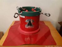 Full view of the red and green metal Christmas tree stand on a wide base with tightening eye bolts.