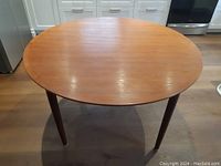 Table in round configuration showing teak veneer top and tapered legs.