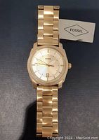 Front view of new men's Fossil watch in gold tone showing dial, hands, and date window with original tag.