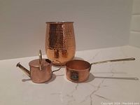 Photo showing the three copper items: mule mug, miniature pot, and miniature watering can arranged on a flat surface.
