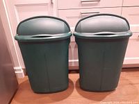 Two green Rubbermaid bins with retractable lids, positioned side by side, showing exterior front view.