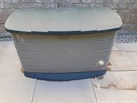 Closed view of the Rubbermaid outdoor storage bin showing beige body and dark green lid with visible wear and fading.