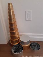 Four sets of stackable collapsible boxes in gold and silver finishes, each set containing 12 round boxes that nest within each other. One gold bottom box has a dent.