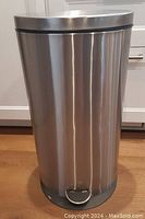 Front view of cylindrical stainless steel garbage bin with closed lid and foot pedal at base