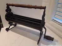 Front side view of the vintage cast iron log roller on countertop showing the overall shape and wooden handle.