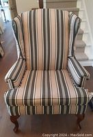 Front view of the wingback chair showing vertical striped fabric upholstery and curved wooden legs with some wear.
