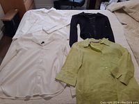 Four tops laid flat on a surface: white Liz Claiborne shirt, black zip-up jacket, white blouse, light green blouse.