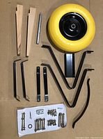 Photo of the wheelbarrow assembly kit components including run flat tire, wooden handles, metal frame parts, and hardware on cardboard