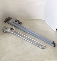 Photo of 36-inch pipe wrench and 24-inch adjustable wrench lying on floor. Pipe wrench is gray, adjustable wrench is chrome-colored.