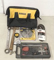 Photo showing DeWALT tool bag with laid out tools including a hammer, wrench, saw blade, screwdriver set, measuring tape, and sandpaper roll.