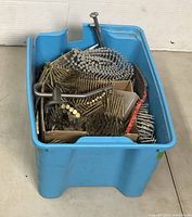 Blue plastic bin filled with various collated nail strips and loose nails of different sizes and finishes.