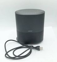 Black Bose Home Speaker 450 smart speaker with attached power cord placed on white surface, shown front and top.