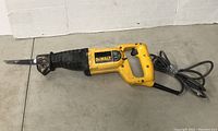 Full side view of yellow DEWALT reciprocating saw with cord wrapped and taped, showing entire tool with blade attached on a concrete floor.