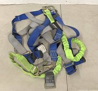Top-down photograph showing the Guardian fall protection harness laid out with visible blue, gray and green straps along with metal buckles and hooks.