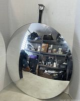 Photo of large round dome mirror with convex reflective surface showing distorted reflection of room and shelving.