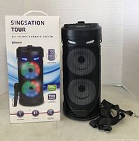 Front and side view of Singsation Tour Karaoke System box showing feature info including Bluetooth, remote control, and wireless microphone compatibility. System includes Bluetooth connectivity and features colorful LED lights on speakers.