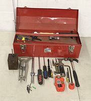 Red metal toolbox open with various tools inside and arranged outside including screwdrivers, hammer, wrenches, pliers, and measuring tool.