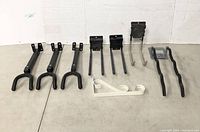 Photo of 11 assorted metal hooks and hangers in black, gray and white finishes, displayed against a wall.