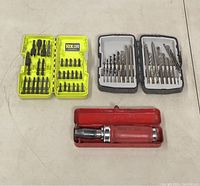 Tool sets including screwdriver bits in yellow case, two drill bit sets in black and clear cases, and red-handled ratchet screwdriver in metal case.